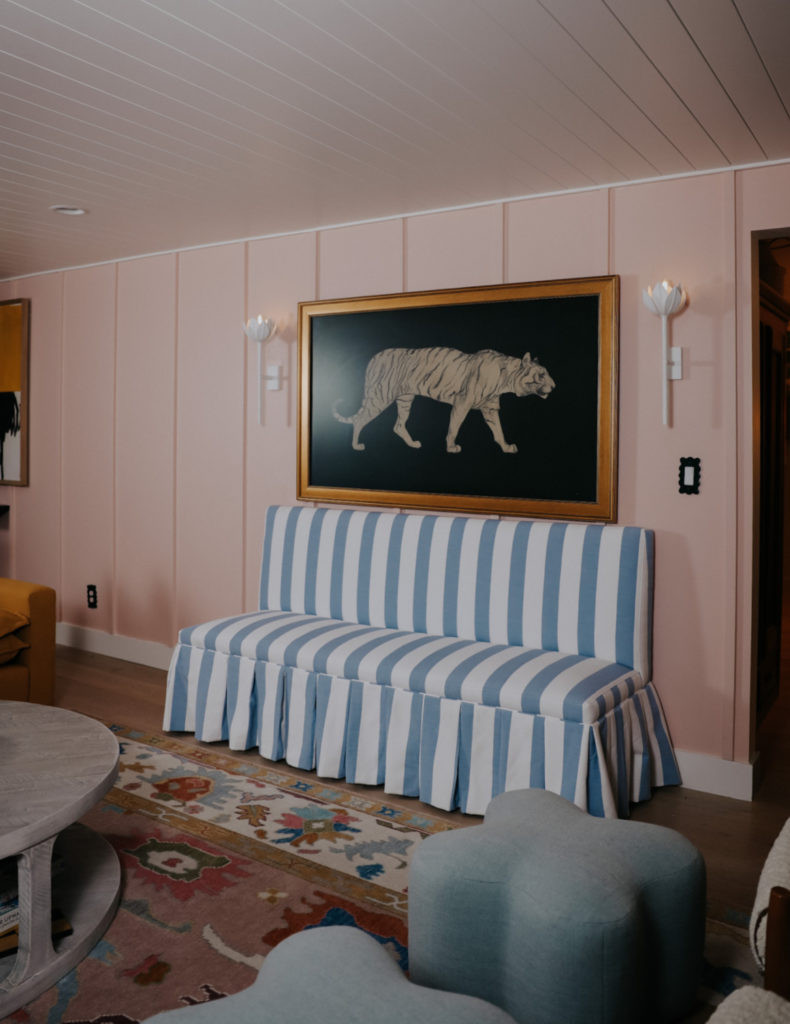 A light-colored pleated bench sits beneath a Samsung Frame TV displaying tiger art. Two wall sconces flank the TV.