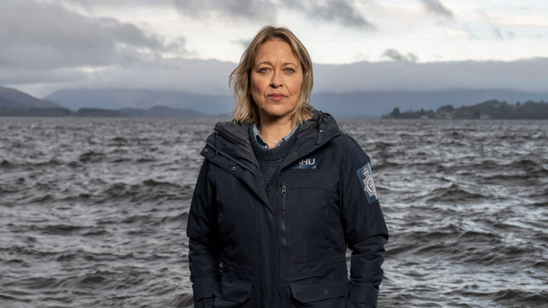 DI Annika Strandhed stands solemnly in front of a grey and choppy sea in the Annika television show.