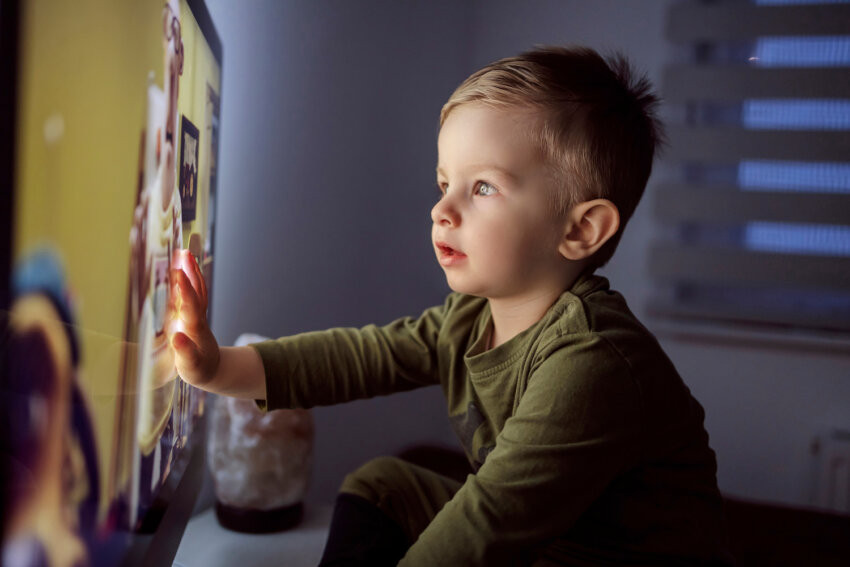 A child sitting very close to a television screen.