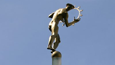 A bronze statue of a muscular nude man holding a ring of fire representing the Sun. He stands atop the world.