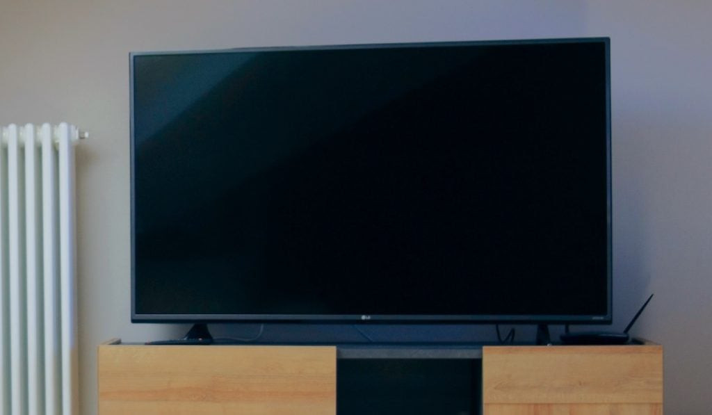 An LG Smart TV turned off, standing on a wooden drawer with a radiator next to it.