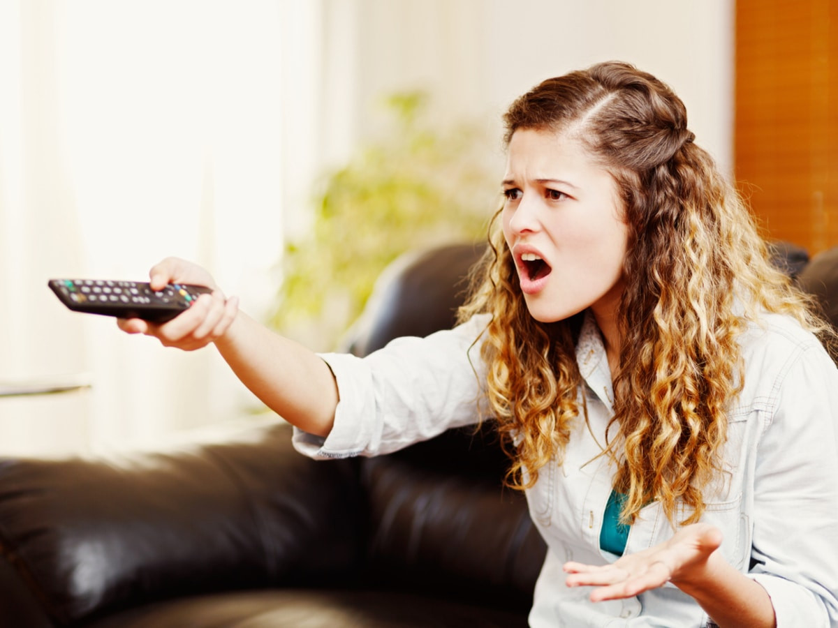 Upset woman pointing remote at TV